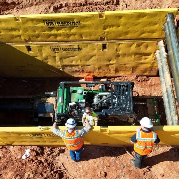 Workers Operating Boring Machine in Trench Box Construction workers operating horizontal boring machine inside trench box