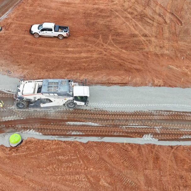 Repeat - Soil Stabilizer Spreading Material Top-down view of soil stabilization operations on red clay construction site