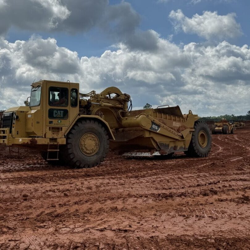 CAT Scraper Vehicle at Construction Site CAT scraper vehicle on red clay construction site under partly cloudy skies