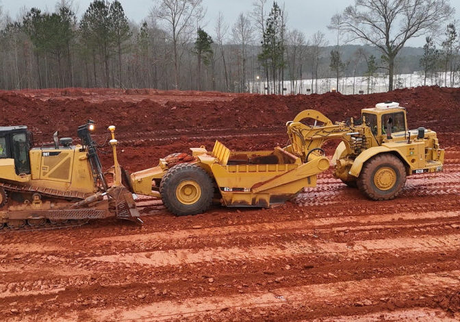 Bulldozer and Scraper Working Together CAT bulldozer towing a scraper on red clay surface during earthmoving operations