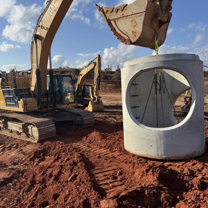 Excavator Lifting Concrete Manhole Section Excavator lifting large concrete manhole section at construction site under blue sky