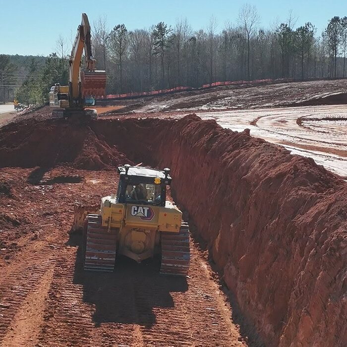Bulldozer in Excavated Trench with Excavator CAT bulldozer operating in a deep red clay trench with an excavator above at a construction site