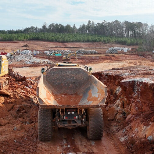 Rear view of a large dump truck in an excavated red clay trench at a construction site